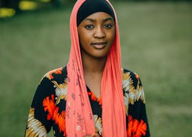 A young woman outdoors, wearing a vibrant scarf and floral dress, exuding confidence.