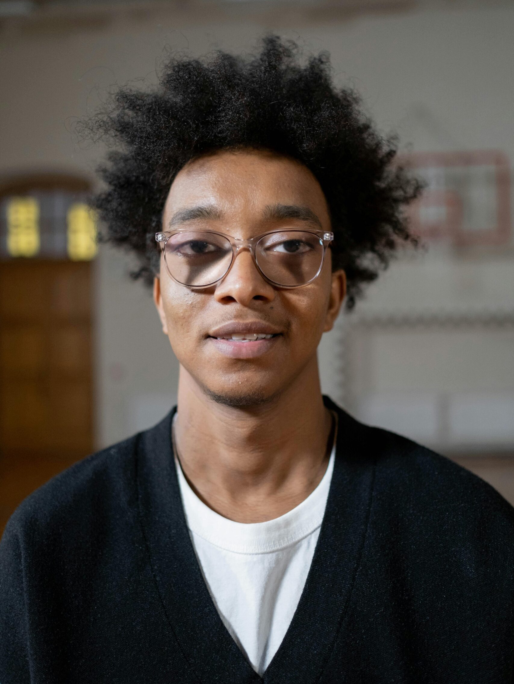 Young man with glasses and afro hair smiling indoors. Casual portrait capturing a relaxed vibe.
