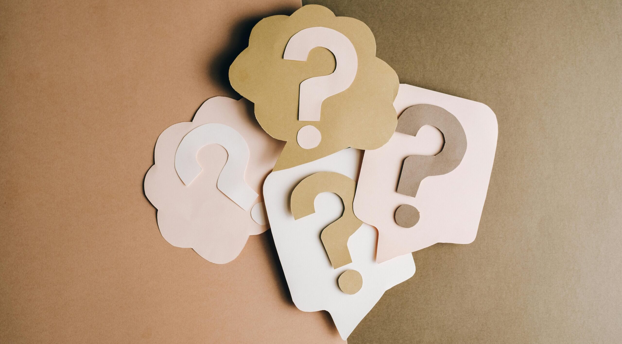 Question mark cutouts in layered paper craft style on a brown backdrop, conceptual art.